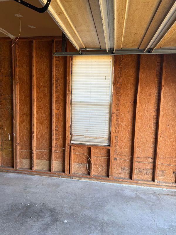 Interior garage view; wooden frame walls, concrete floor, window with blinds.