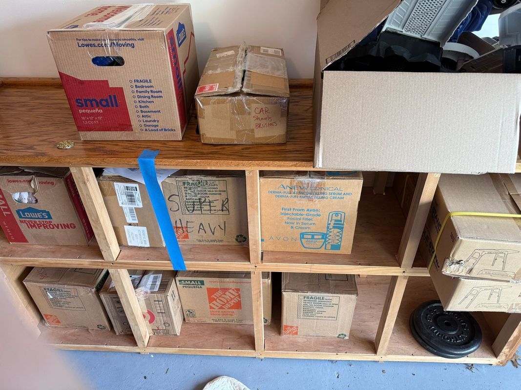 Boxes on a wooden shelf in various sizes and conditions, some taped, indoors.