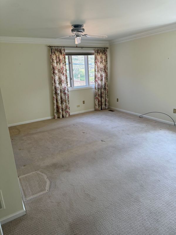 Empty room with beige walls, patterned curtains, and dirty carpet.