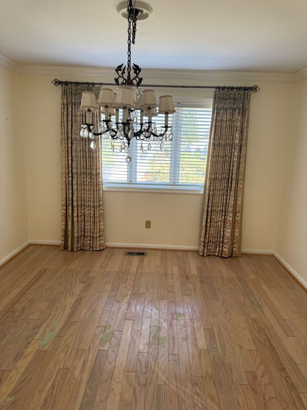Empty dining room with hardwood floors, window, patterned curtains, and chandelier.