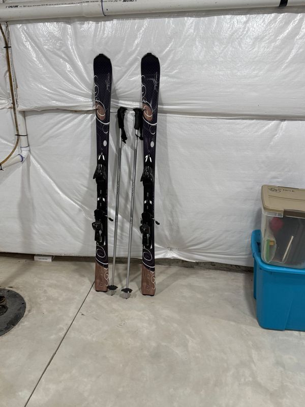 Pair of skis with poles leaning against a wall in a basement.