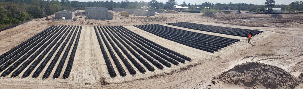 Rows of dark material in a sandy field, likely for agriculture. A person stands in the field.