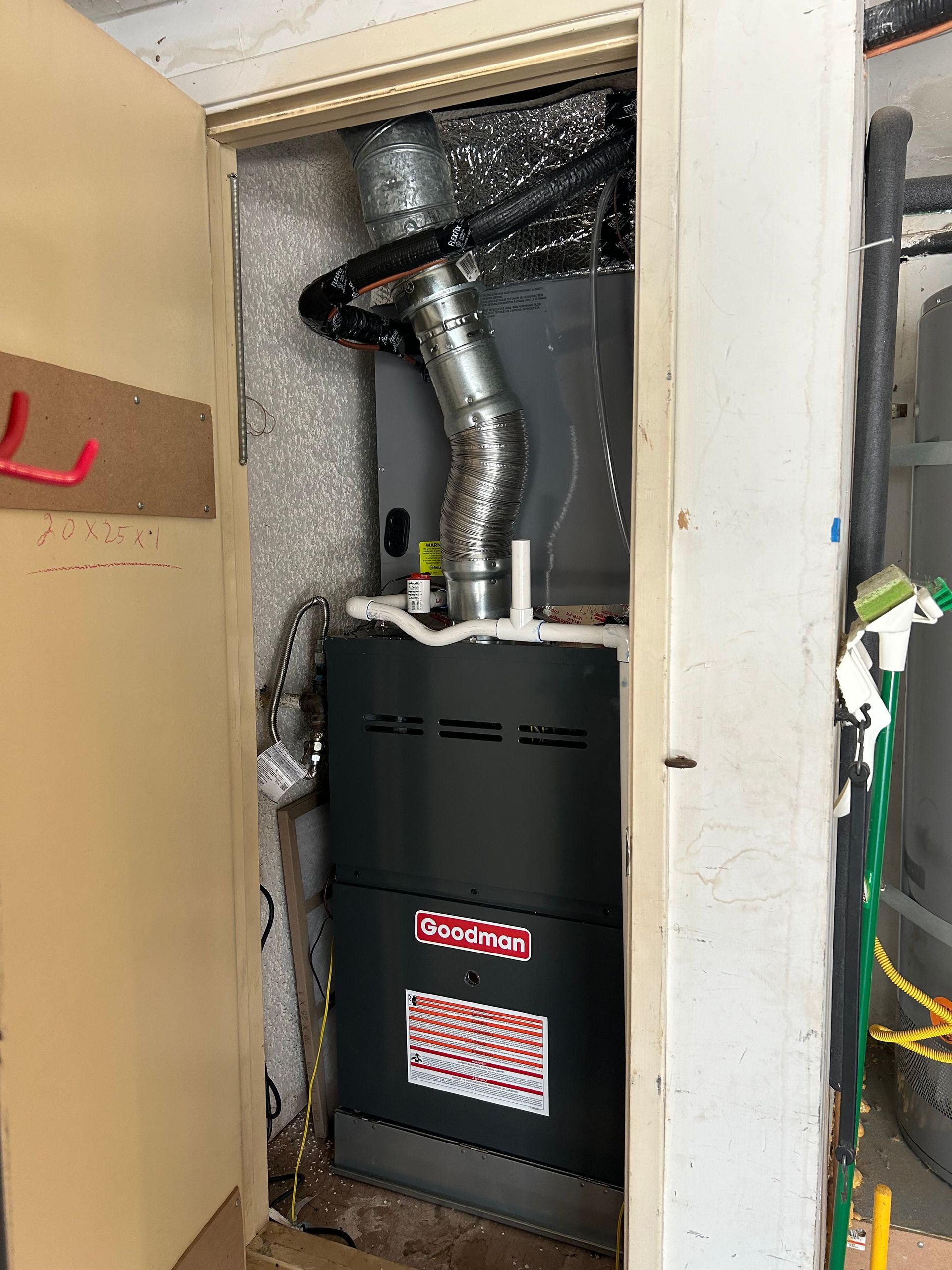 A furnace unit, in a utility closet, with a silver exhaust pipe, gray exterior, and red logo.