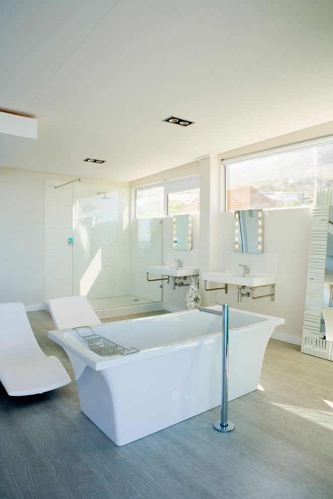 Bright white bathroom with a freestanding tub, two lounge chairs, and large windows.