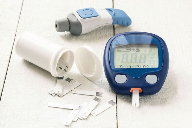 Diabetes blood glucose testing supplies on white surface: meter, test strips, lancing device.