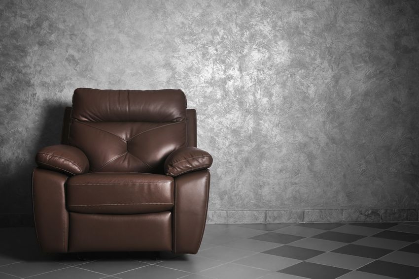 Brown leather armchair against a gray textured wall on a checkered floor.