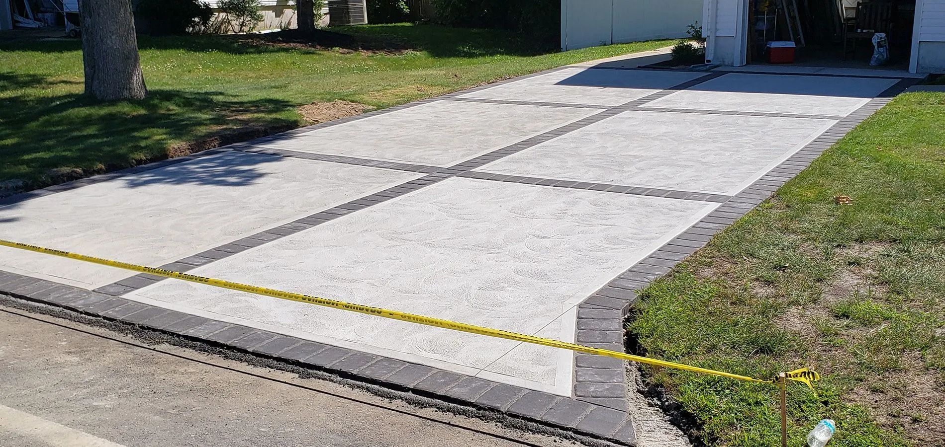Concrete driveway with yellow guide lines leading to a garage, bordered by grass and brick edging