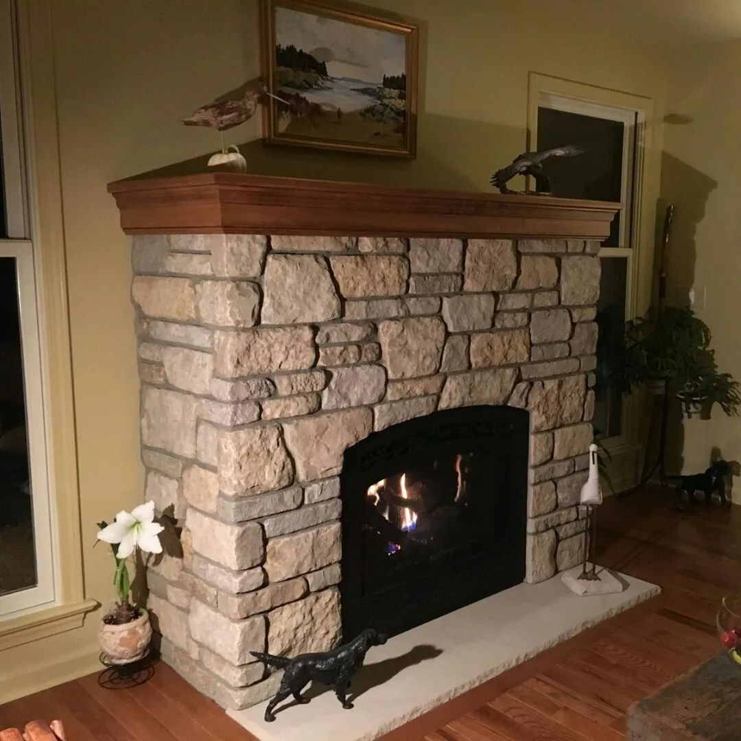 Stone fireplace with a wooden mantel and a small fire burning in a cozy living room.