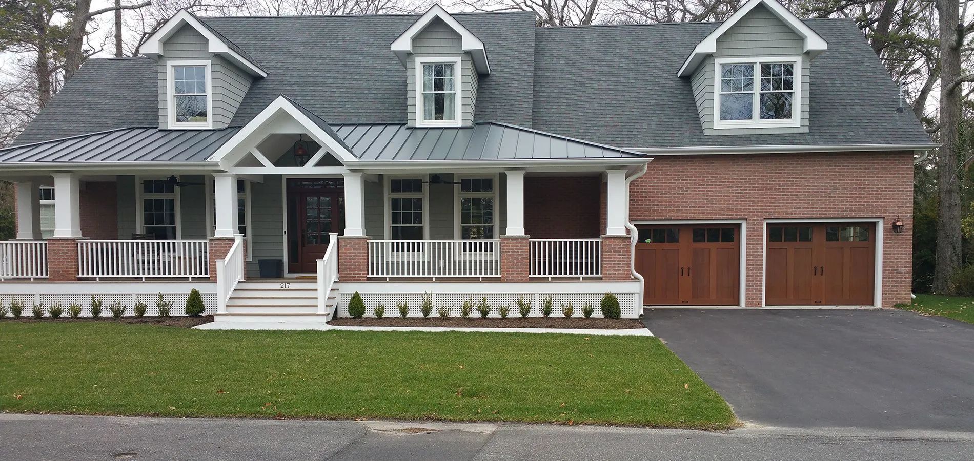 Large gray house with white trim, front porch, dormer windows, and attached brick garage.