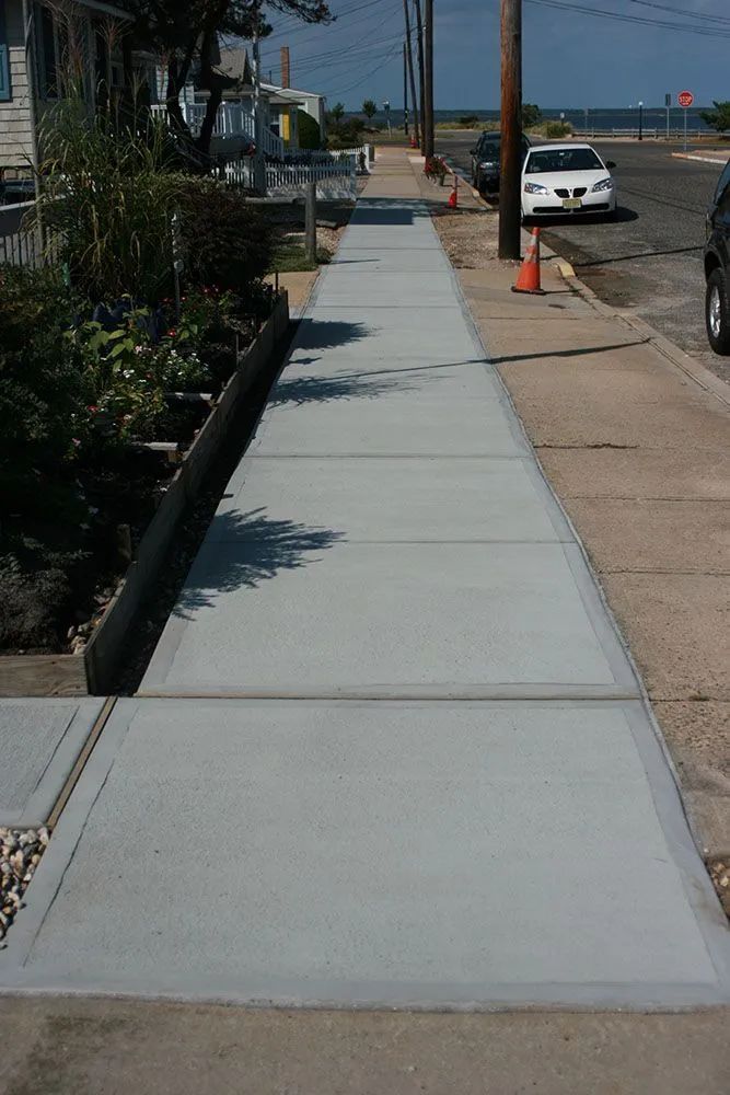 Sidewalk along a residential street with parked cars and an orange traffic cone near the curb.