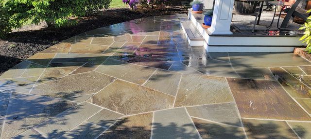 Stone patio with a wet walkway, fountain, and garden shadows in bright sunlight