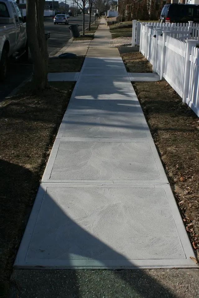 Concrete sidewalk along a residential street beside a white picket fence and parked cars