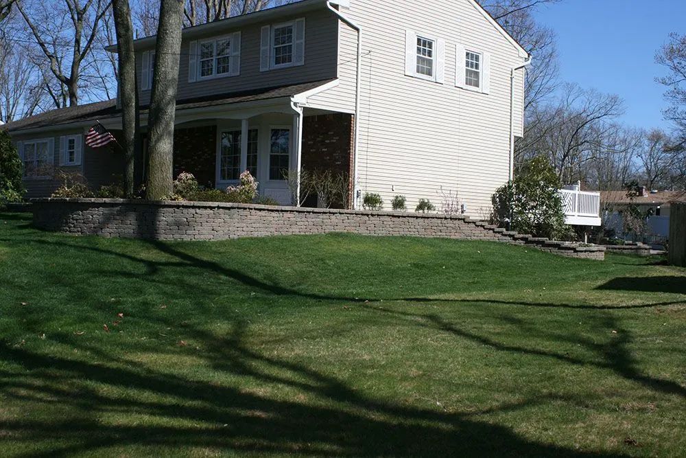 Suburban two-story house with white siding, front porch, and large grassy yard on a sunny day