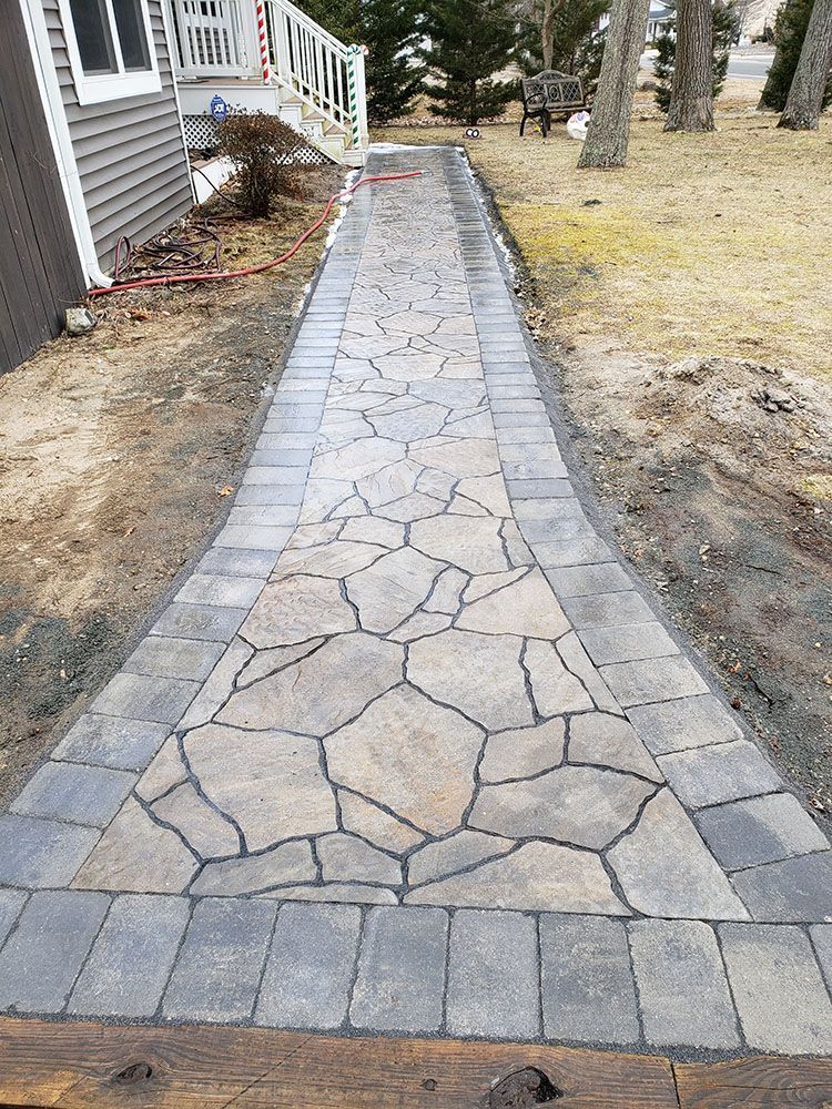 Stone walkway with gray border pavers leading beside a house through a yard