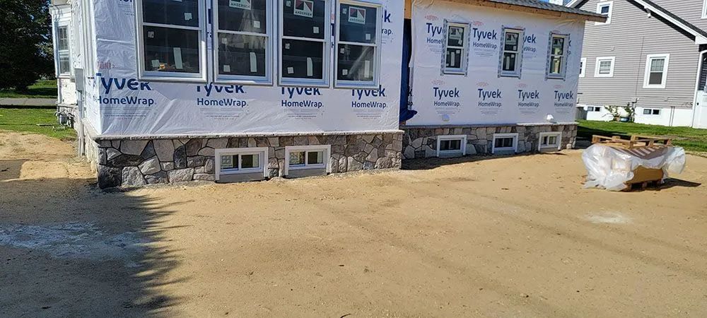 Partially built house wrapped in white house wrap on a dirt lot with a dumpster nearby