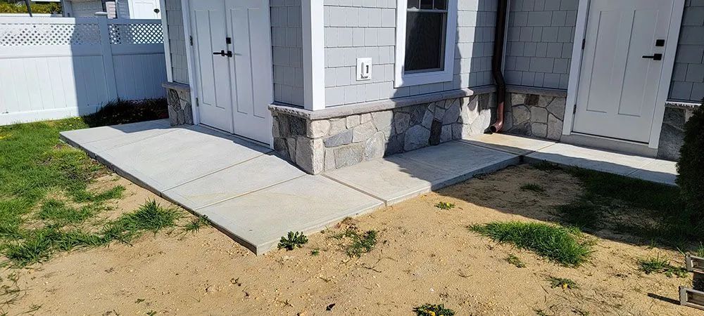 Concrete ramp leading to a house entrance beside a stone foundation and open white doors.