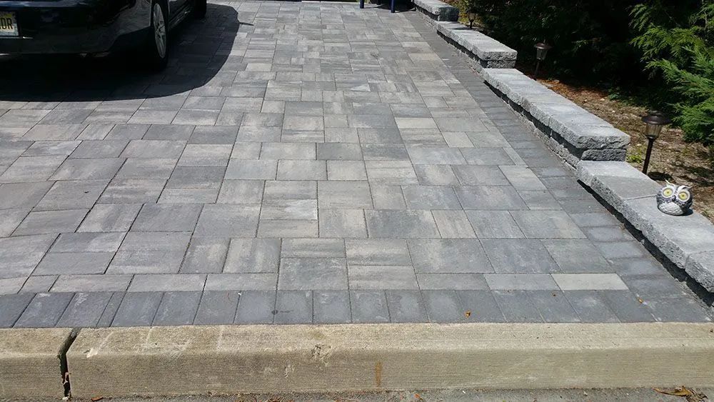 Paved driveway with gray stone pavers beside a curb and parked car