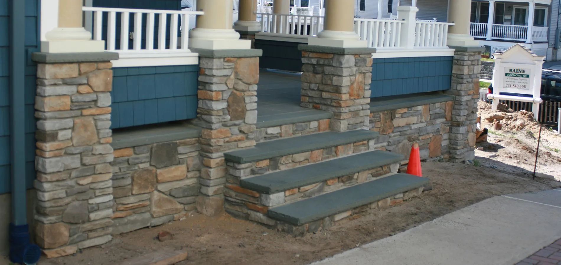 Front steps under construction beside a house, with stone pillars and a traffic cone
