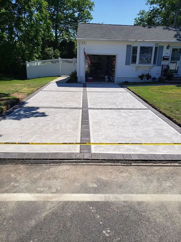 Freshly poured concrete driveway leading to a garage attached to a white house.