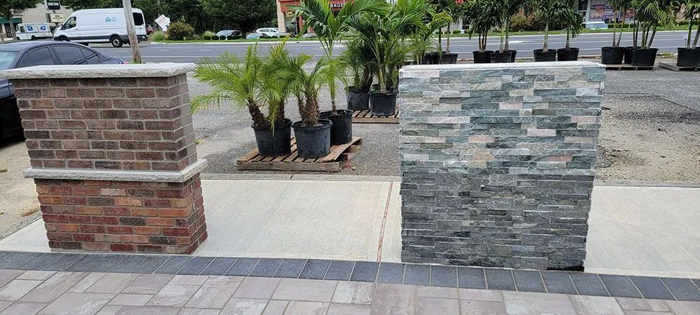 Two brick columns with stacked stone tops beside a sidewalk and parking lot