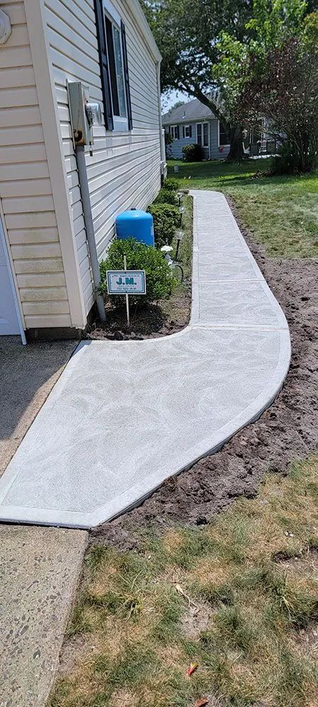 White concrete walkway curving alongside a beige house beside a blue utility box and lawn.