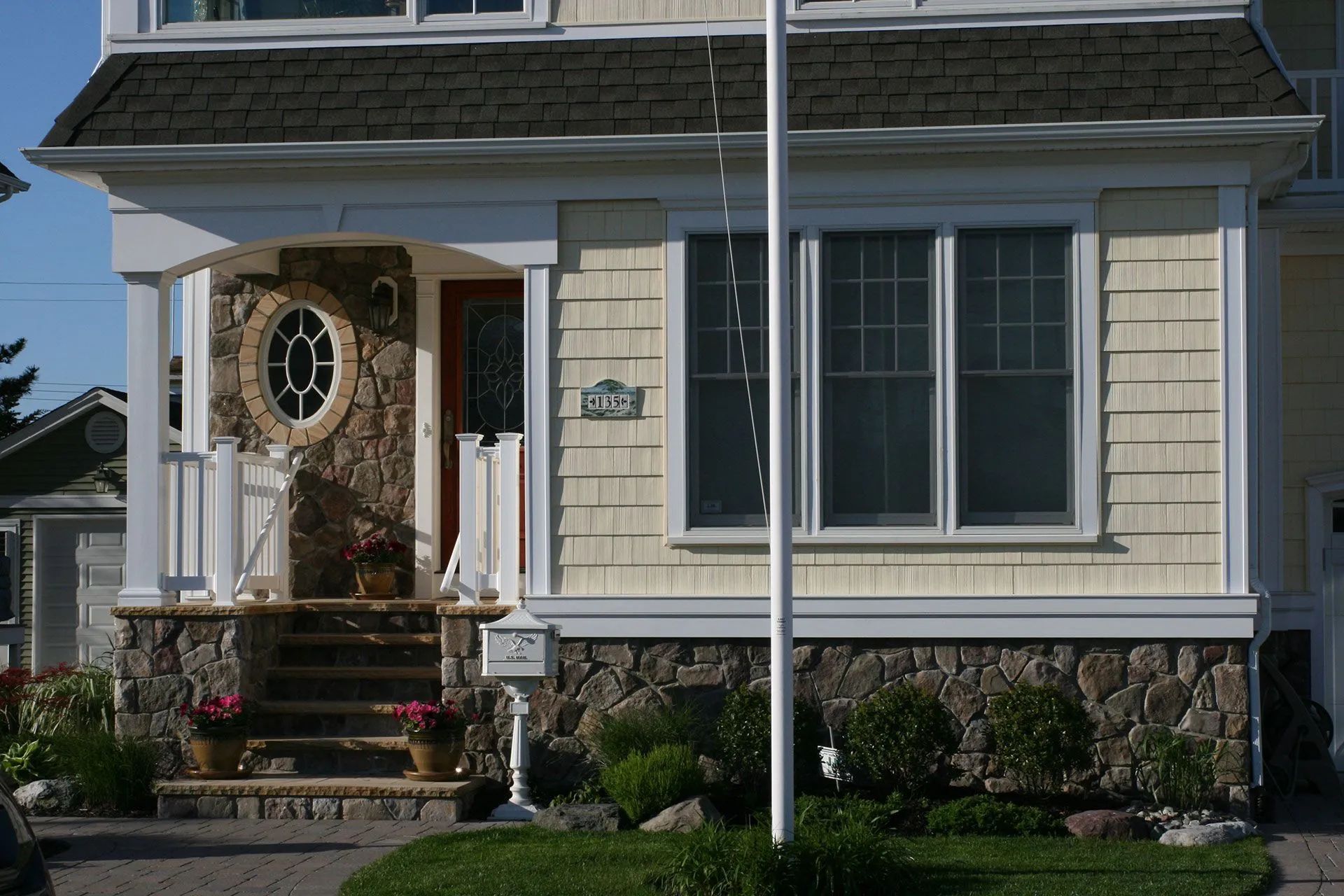 Front porch of a beige house with white trim, a red door, and large window, seen behind a flagpole.