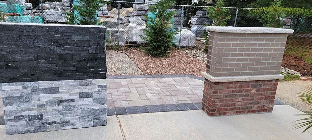 Stone and brick retaining walls beside a paved walkway in a landscaped outdoor area