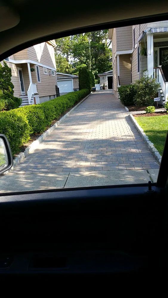 View from a car of a paved walkway between apartment buildings and hedges on a sunny day