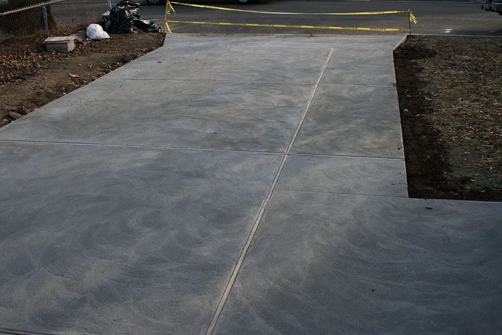 Concrete driveway leading to a street, with a yellow barrier and soil on either side.