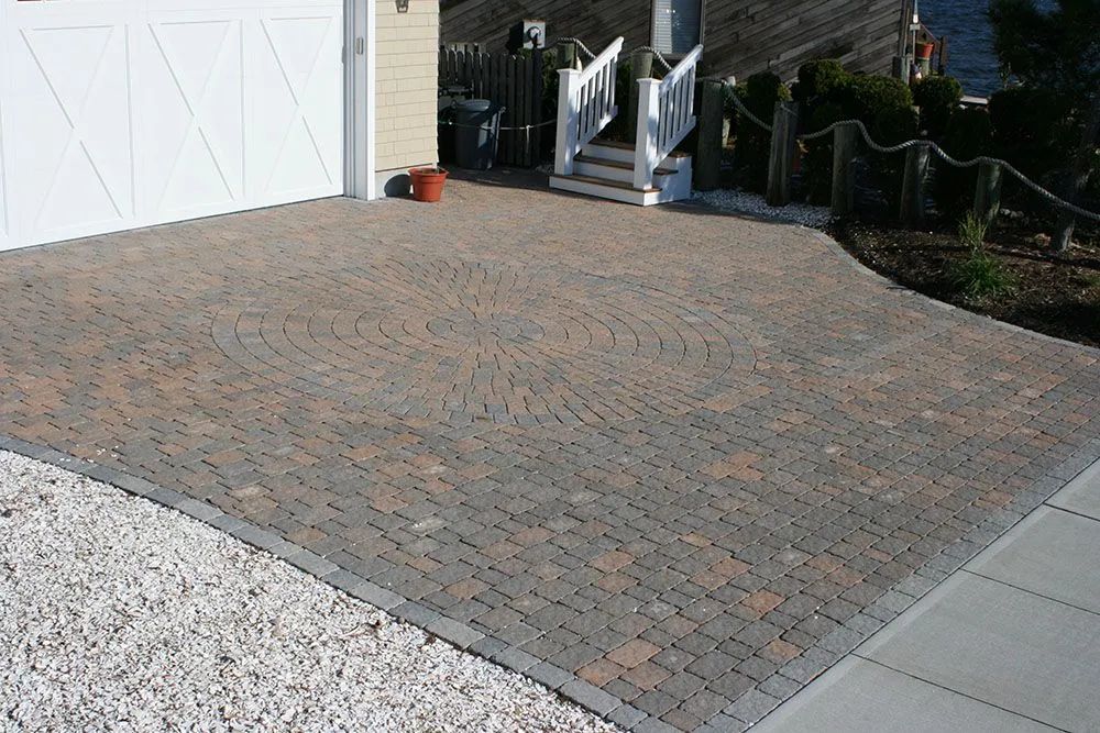 Brick-paved driveway beside a white garage and gravel path in a residential yard