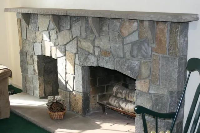 Stone fireplace with two openings, a log inside, and a chair nearby in a living room