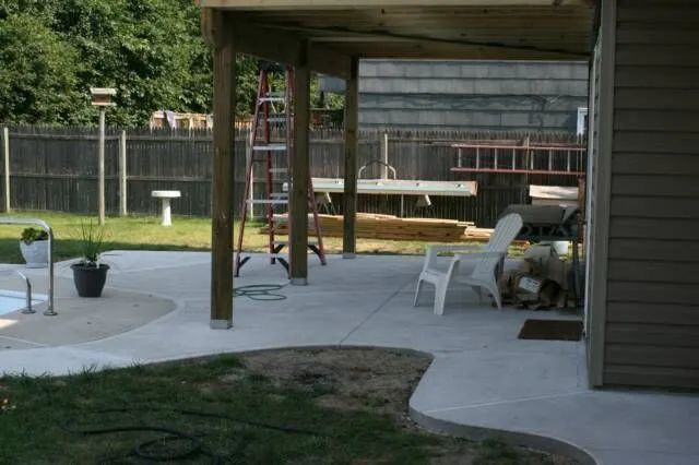 Backyard patio with covered seating area, white chairs, grill, and fenced yard.