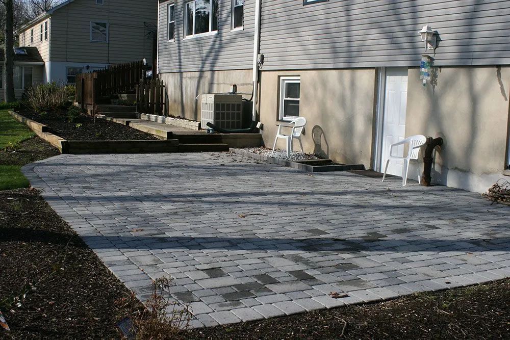 Backyard patio with a large stone paver section beside a house and steps leading to a deck