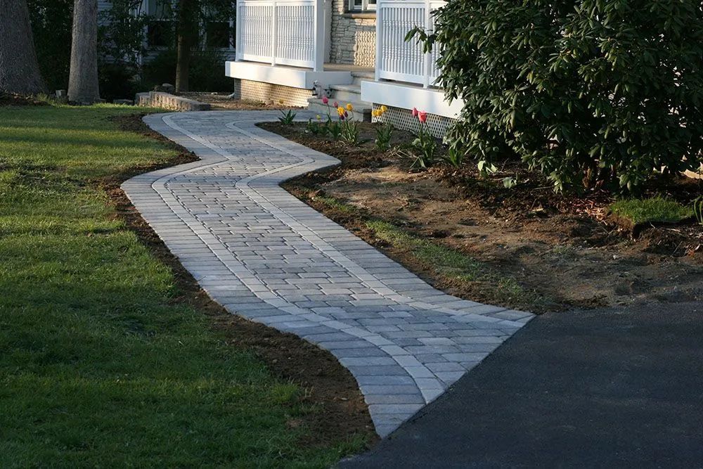 Winding white stone walkway leading to a house entrance through a green front yard.