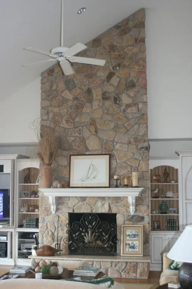Living room with a tall stone fireplace, white mantel, and ceiling fan