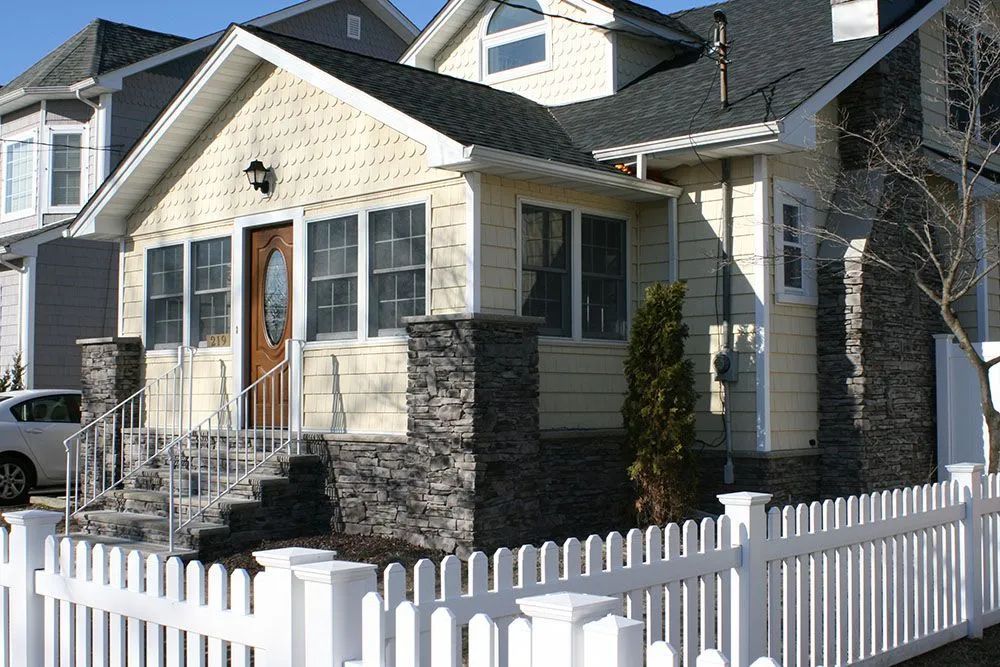 Suburban house with beige siding, white picket fence, and stone porch columns