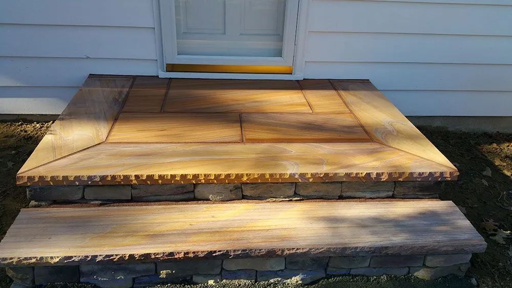 Wooden front porch steps leading to a white house door, lit by sunlight.