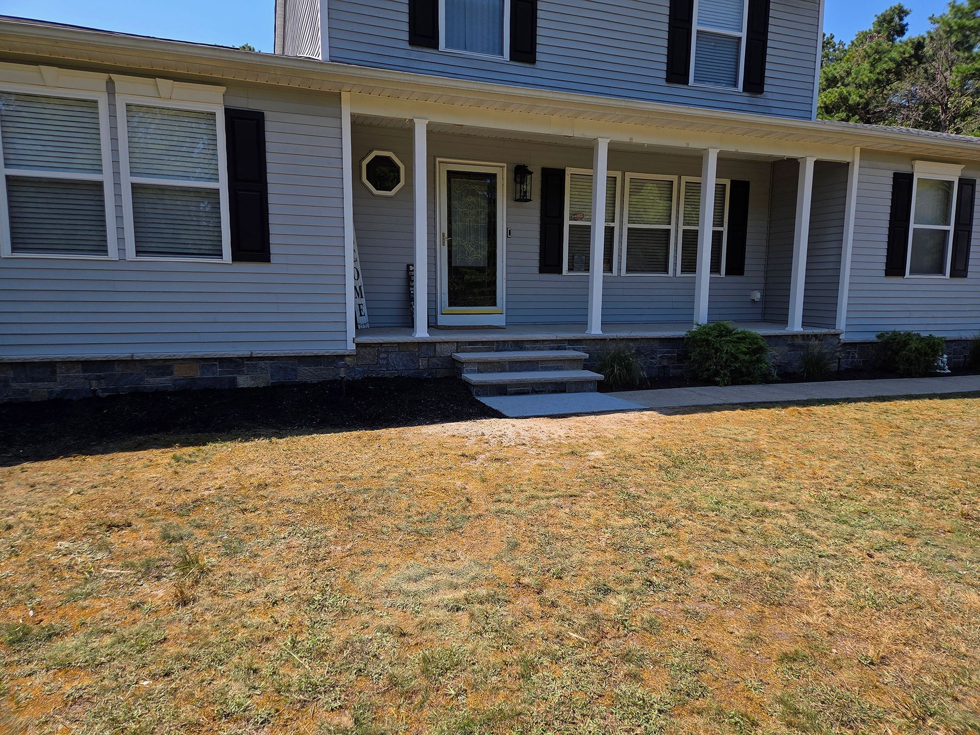 Suburban house with white siding, front porch, and a dry lawn in the foreground