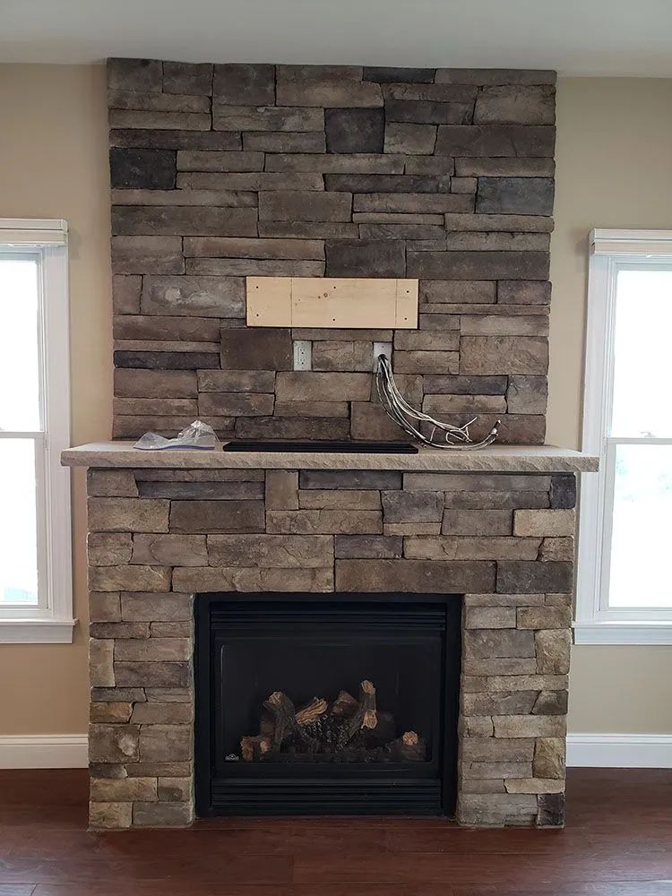 Stone fireplace with a white mantel and framed opening between two windows in a living room
