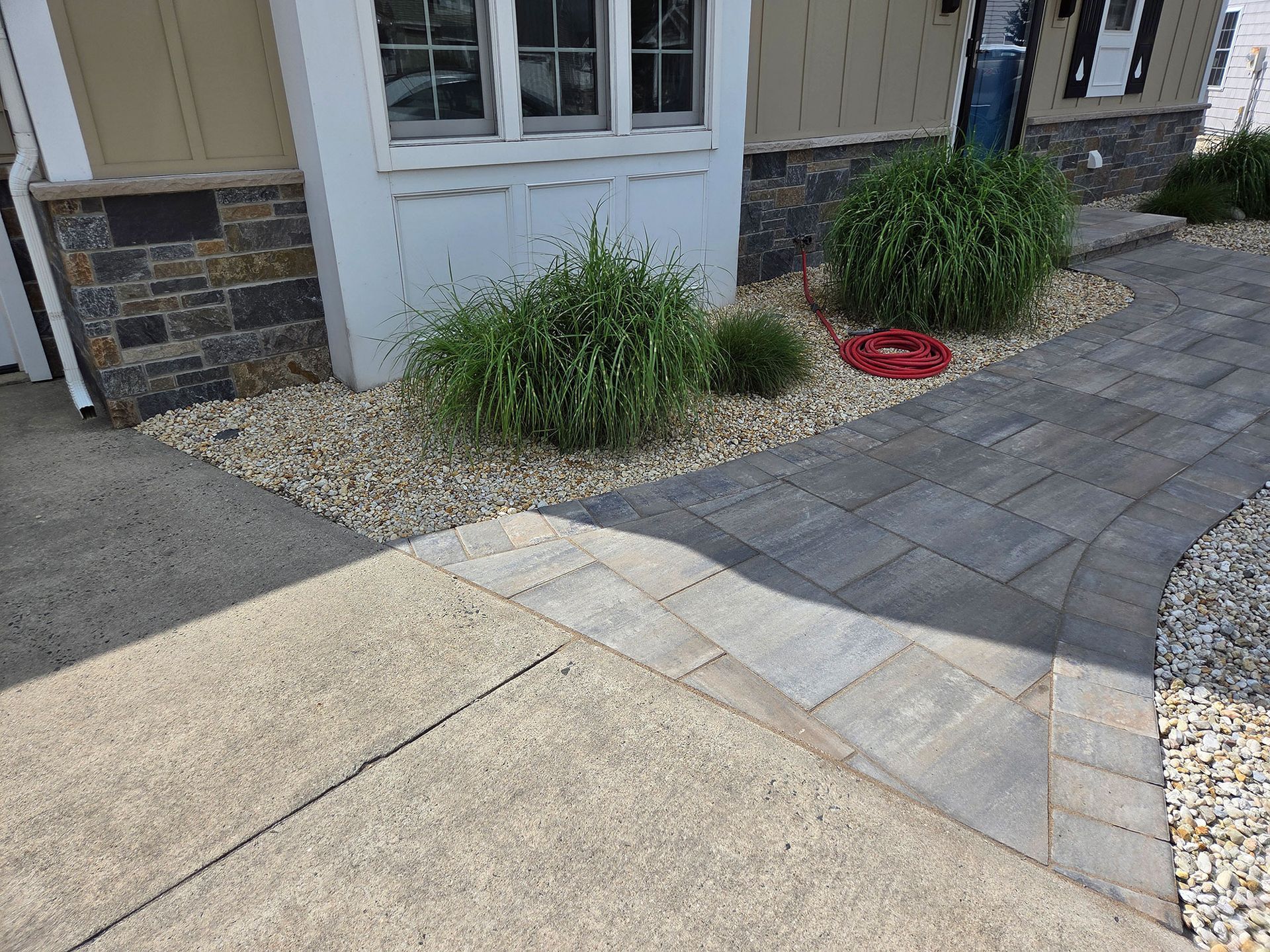 Walkway with paver path, concrete slab, shrubs, and stone mulch beside a house entrance