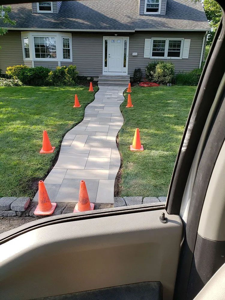Front walkway lined with orange cones leading to a house with a gray exterior and white door