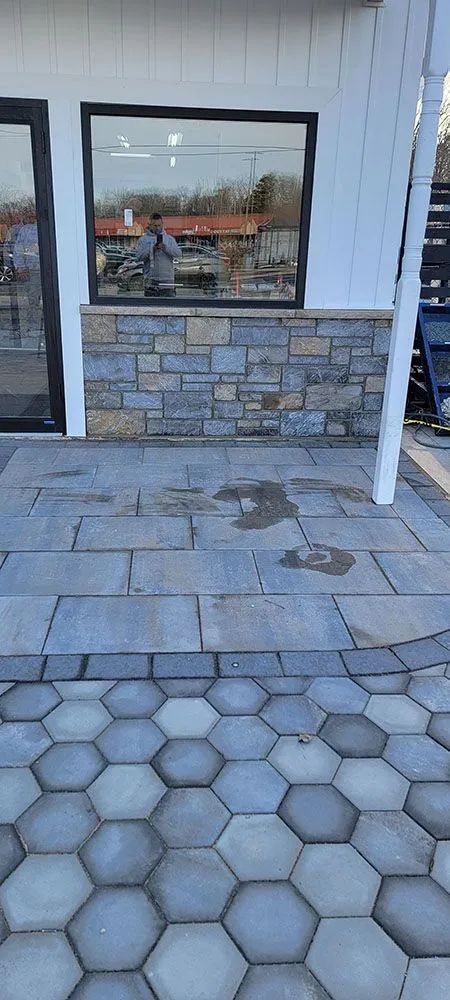 Hexagonal stone walkway leading to a building entrance with a stone-faced wall and large window.