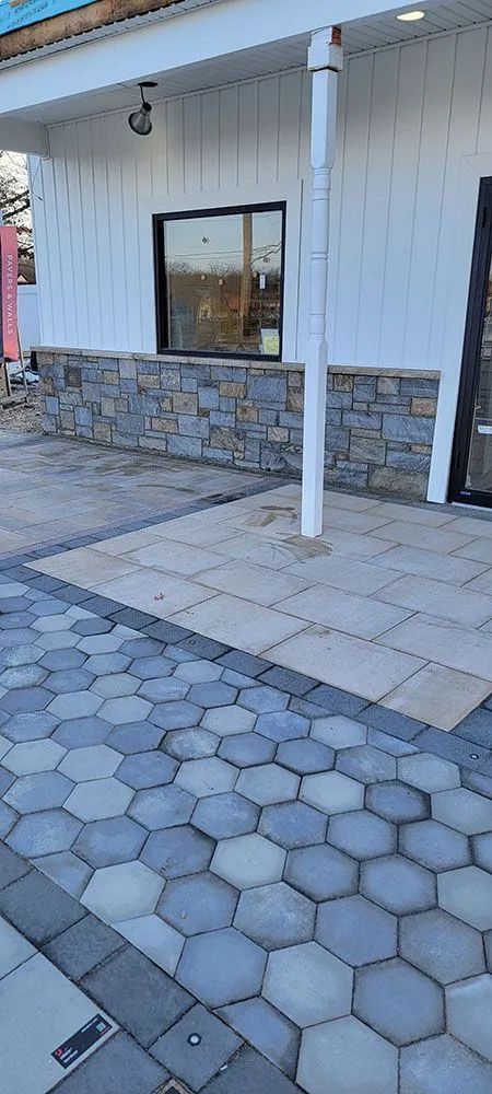 Exterior of a building with white siding, stone base, window, and paved sidewalk with hexagonal pavers
