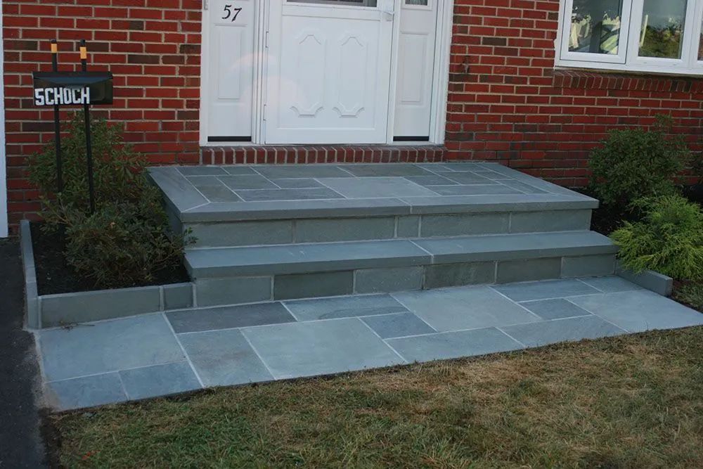 Front steps of a brick house with gray stone walkway and a small mailbox in the yard