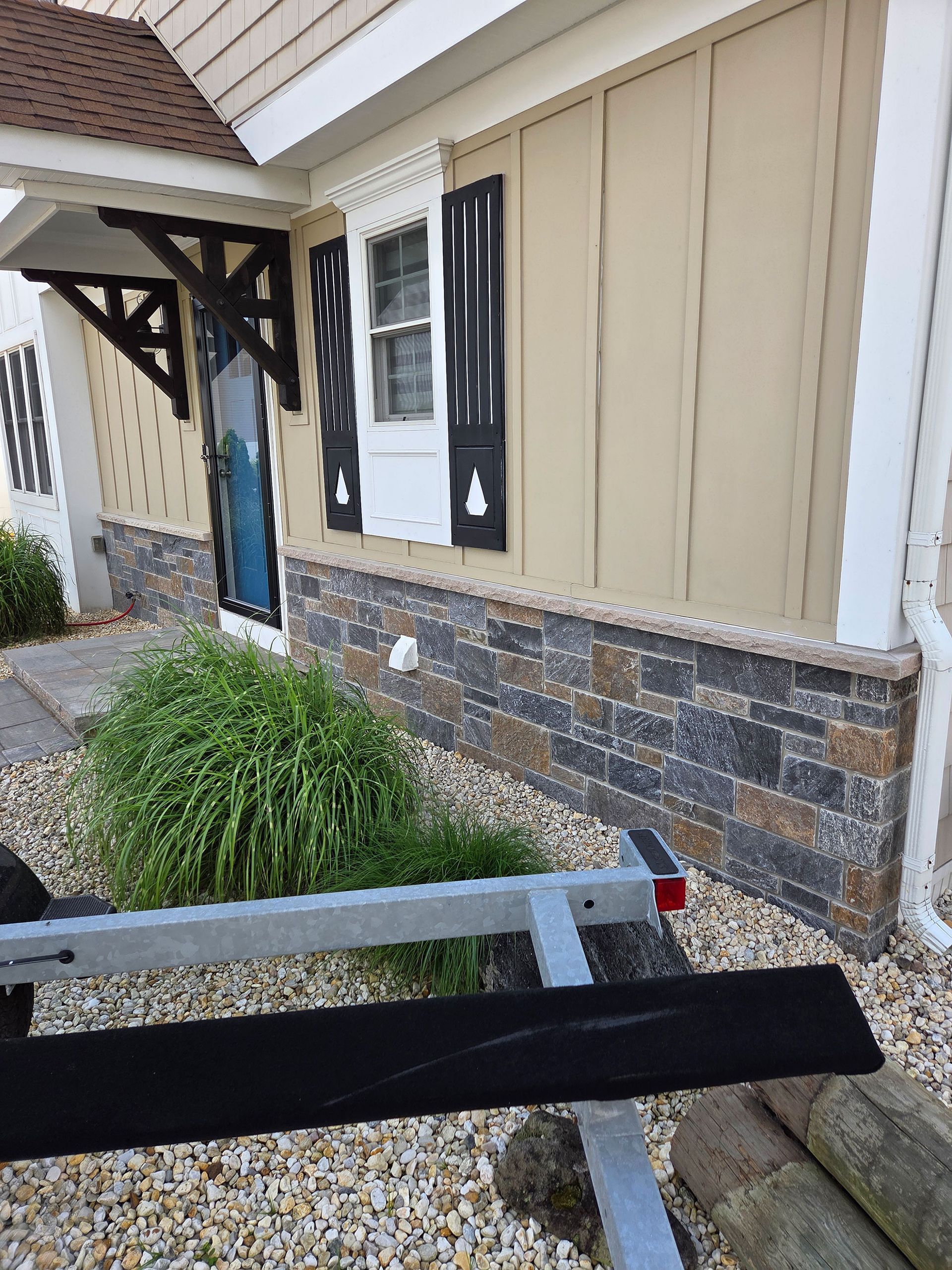 House exterior with beige siding, stone lower wall, window, and a ramp railing in the foreground