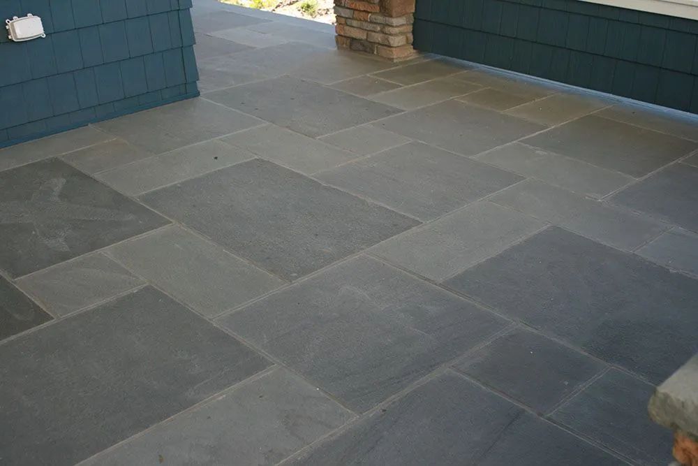 Gray stone patio tiles beside blue walls and a brick column.