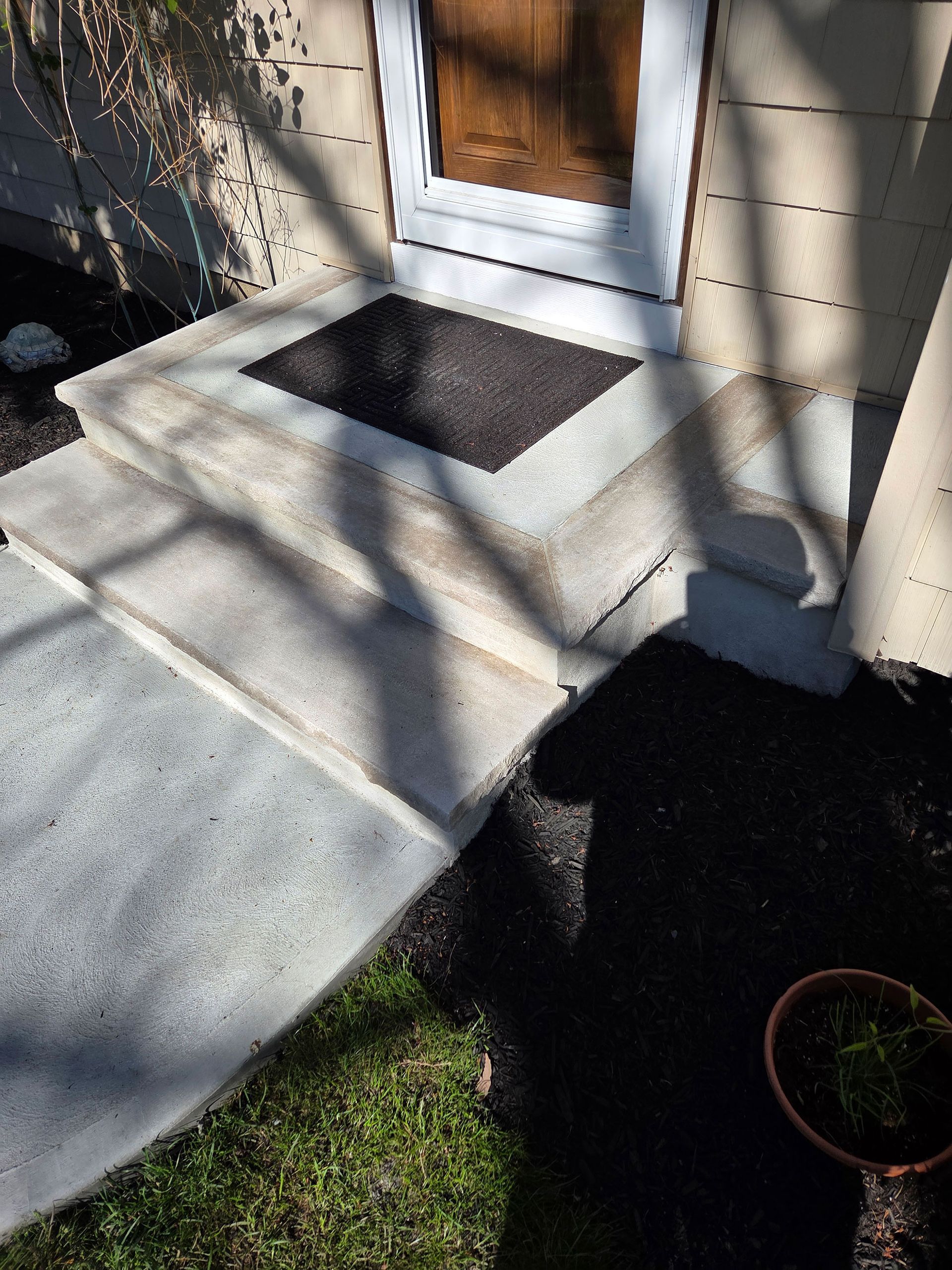 Concrete ramp and small step leading to a front door, with shadows across the walkway.