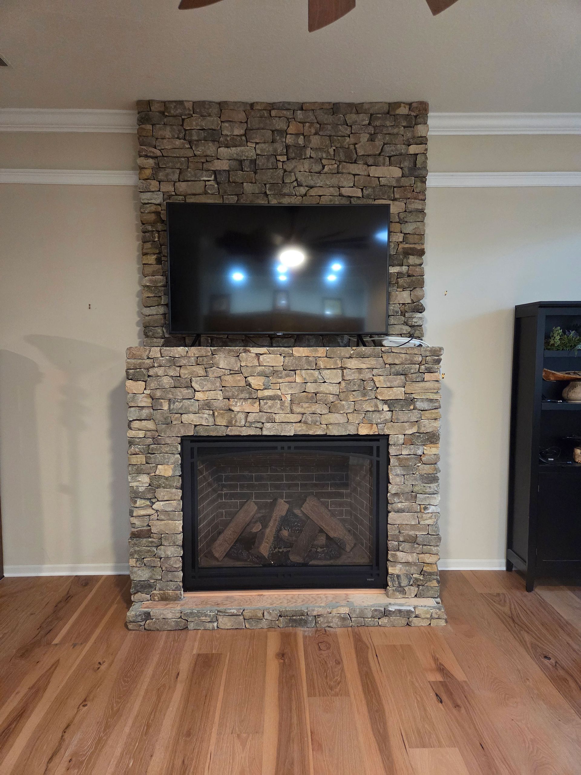 Living room stone fireplace with mounted TV and hardwood floor