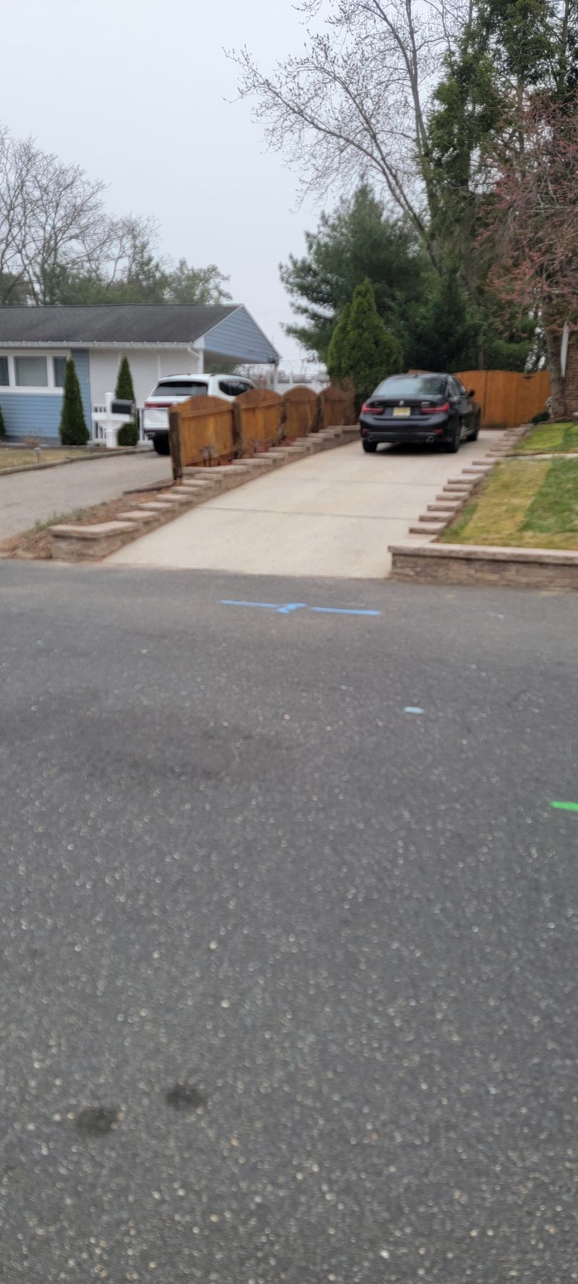 Suburban driveway with parked SUV, white house, and wooden fence on a quiet street