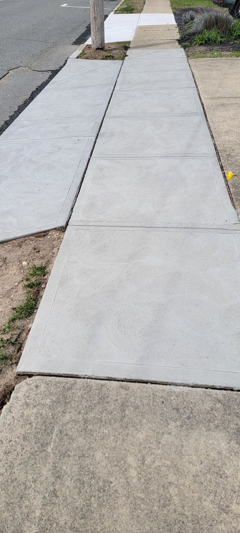 Concrete sidewalk ramp with raised curb and adjacent cracked pavement